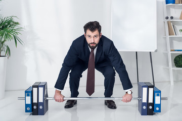 businessman in suit weightlifting folders in office