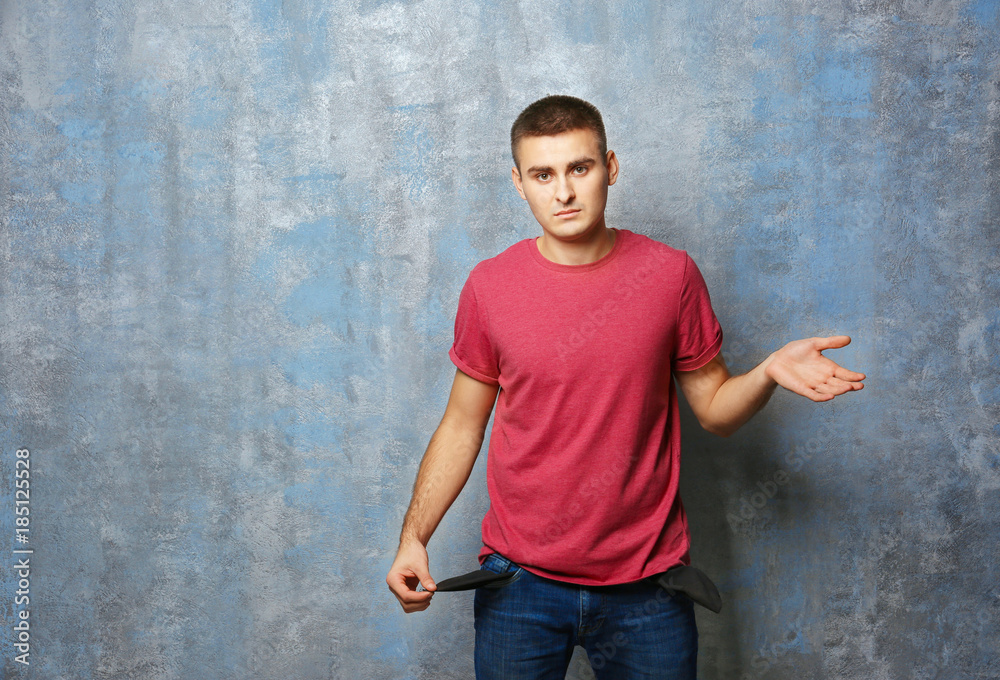 Young man showing his empty pocket on grey background