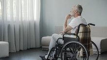 Thoughtful Retired Male Sitting In Wheelchair And Looking In The Window, Disease