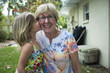 © Cavan Images - Portrait of cheerful grandmother with granddaughter kissing her at yard