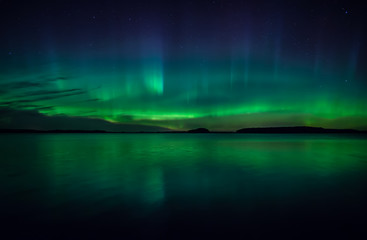 northern lights dancing over calm lake in farnebofjarden national park in sweden