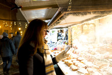Woman Window Shopping On Traditional Christmas Market In Latvia On Cold Winter Day. Woman Looking At Gingerbread In Confectionery At Christmas Market