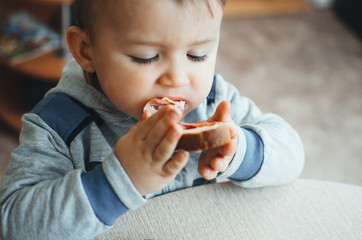 The child is small and cute eating a sandwich with bread sausage and cheese