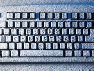 computer keyboard with text merry christmas on buttons covered with snow lit by light