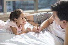 Cheerful Young Father Making A Pinky Swear With His Daughter On Bed