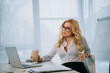 seductive businesswoman holding coffee in paper cup and looking at laptop