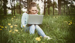 © spaxiax - Young woman with laptop sitting on green grass
