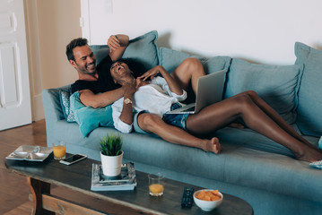 Wall Mural - Happy young couple relaxed at home lying down in the couch on the computer