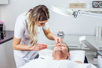 Cosmetologist woman is doing eyebrow modeling for man by wax for epilation. Cosmetological clinic. Healthcare