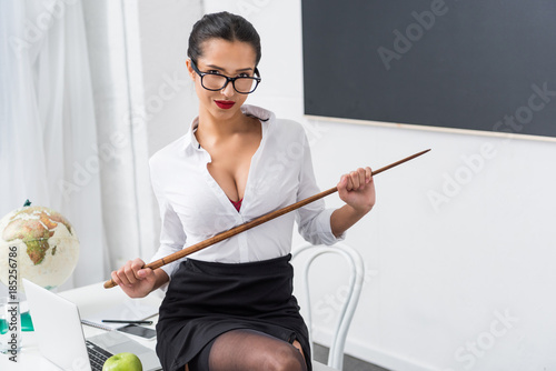 Young Sexy Teacher With Pointer Sitting On Workdesk Young Sexy Teacher With Pointer Sitting On Workdesk