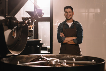 Wall Mural - portrait of smiling coffee roaster standing at roasting machine and looking at camera