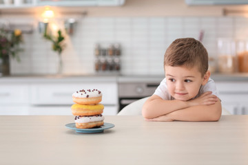 Plate with sweet donuts on table and little cute boy in kitchen