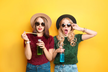 Two hipster girls with drinks on color background