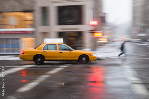Cuadros en Lienzo Panning motion image of a New York City yellow taxi cab in the snow as it passes