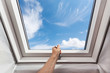 Man open new skylight (mansard window) in an attic room against blue sky