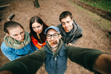 Crazy company have fun outdoor at nature. Four young persons fooling and making funny selfie portrait. Men and women eat sausages. Group of people mess around. Meat eaters. Odd bizarre mad party time.