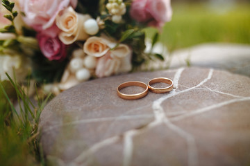 Golden wedding rings with bouquet on the stone background. Wedding decoration outdoors