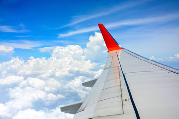 red wing of the aircraft view from airplane window seat flying in the blue sky with white clouds background, copy space