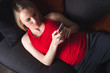 © LALSSTOCK - A happy pregnant woman in a red T-shirt and gray pants lies at home on the couch in the evening and holds a mobile phone. A woman is shopping by phone. Online shopping