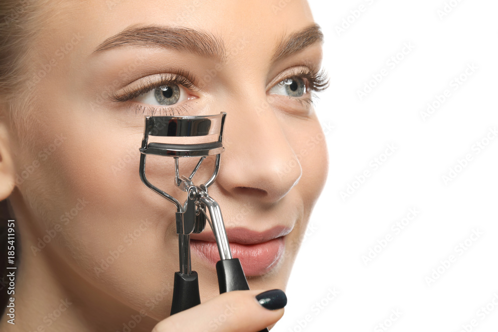 Beautiful young woman with eyelash curler on white background