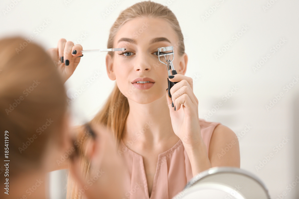 Beautiful young woman using eyelash brush and curler at home