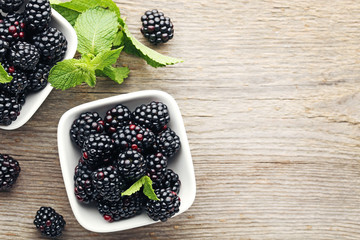 Ripe and sweet blackberries in bowls on wooden table