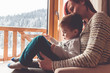 Mother and her son sitting in a comfortable chair with tablet next to the window with look at snow covered mountain.