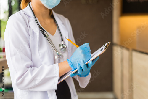 Fotomural woman doctor in white coat with stethoscope and blue glove write report by pencil in a notebook on blur background of hospital