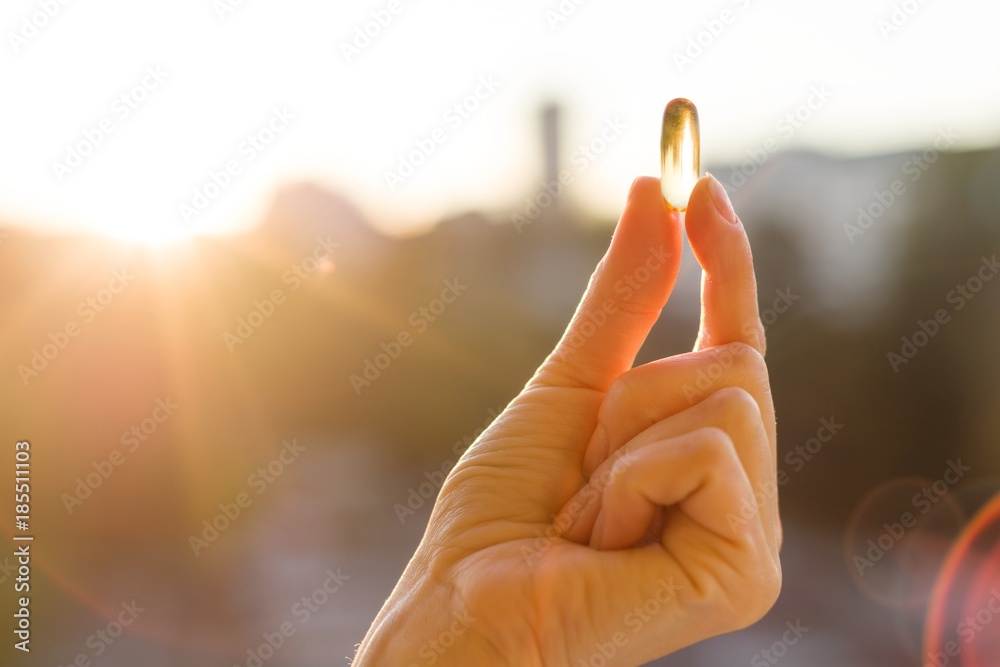 Obraz na płótnie Hand of a woman holding fish oil Omega-3 capsules, urban sunset background. Healthy eating, medicine, health care, food supplements and people concept w salonie