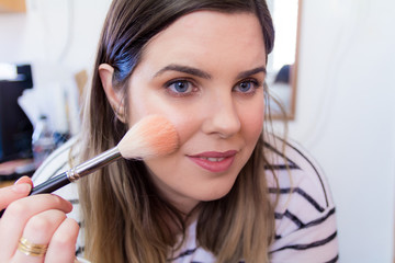 Woman applying makeup in her bedroom