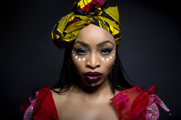 Wall Mural - Black female showing African pride by wearing Nigerian traditional clothing and tribal makeup or face painting.  The model is shot in studio in modern vogue fashion style.