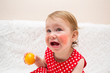 cute little girl a child with eczema or an allergy on her cheeks because of consuming citrus fruits, sits on a sofa with tangerines