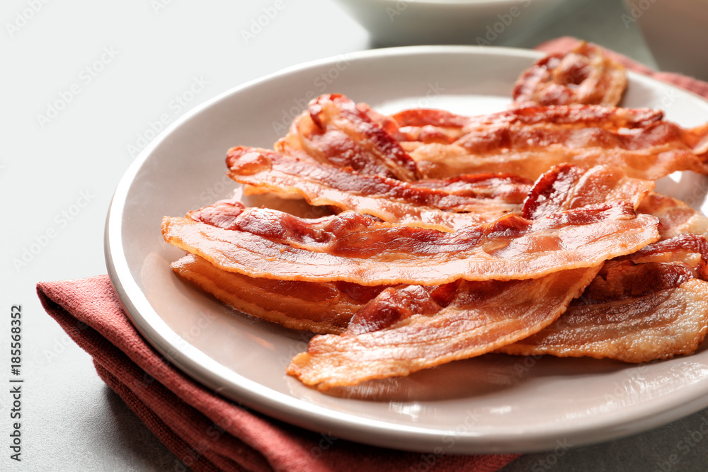 Plate with cooked bacon rashers on table, closeup