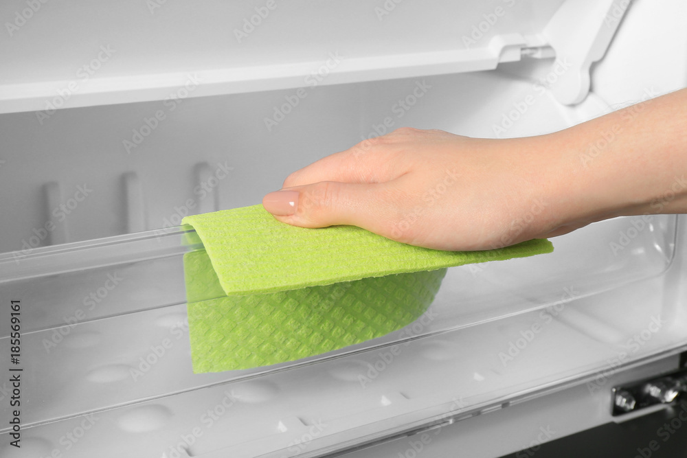 Woman cleaning refrigerator with rag, closeup