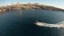 A man in Santa Claus costume rides on jetsurf beside beautiful ocean coast Aerial view