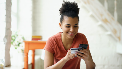 Beautiful happy mixed race woman online banking using smartphone shopping online with credit card at home lifestyle