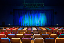 The Auditorium In The Theater. Blue-green Curtain On The Stage. Multicolored Spectator Chairs. Lighting Equipment.