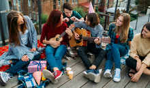 Group Of Friends Listen To Buskers Singing And Playing Guitar And Ukulele At A Roof Top Party. Musician Artistic Lifestyle. Teenagers Leisure