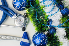 Christmas And New Year Decorations Near Medical Equipment. Neurology Hummer And Medical Stethoscope Lying Near Artificial Snow With Glitter, Toys And Blue Balls On Christmas Tree. New Year In Medicine