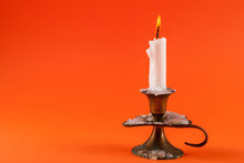 Paraffin Candle Burning In Old Candlestick Isolated On Orange Background And Space For Text