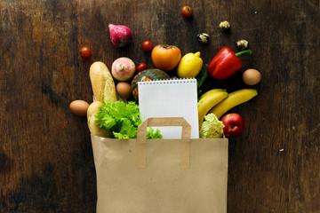 Canvas Print - Paper bag different health food notebook wooden background Top view