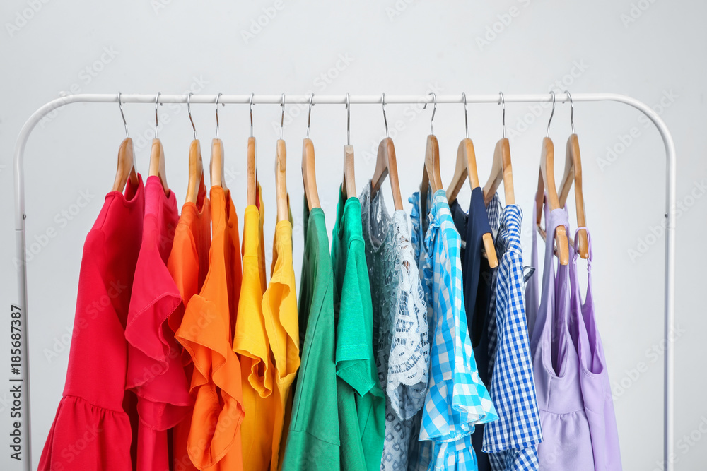 Stylish clothes hanging on wardrobe stand against light background