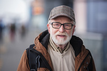 Old Generation. Portrait Of Positive Senior Bearded Man With Glasses Is Standing Outdoors And Looking At Camera With Slight Smile