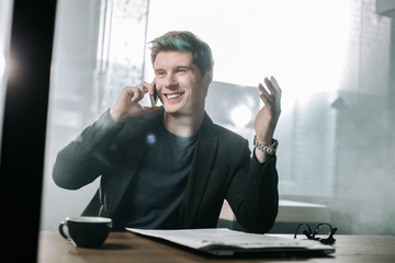 Aufkleber - Portrait of cheerful male telling by mobile while sitting at desk in modern office. Rest and profession concept