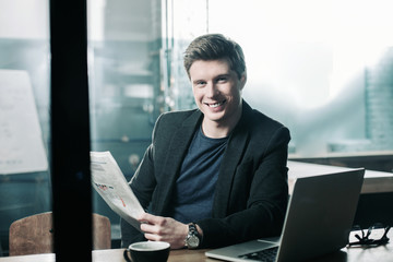 Aufkleber - Portrait of cheerful young man reading newspaper during break at table in office. Relax and occupation concept