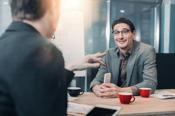 Aufkleber - Portrait of smiling bearded man telling with comrade while sitting at table in office. Profession and conversation concept