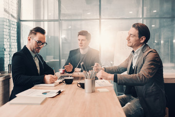 Aufkleber - Portrait of smiling bearded man writing in copybook while speaking with happy partners. They situating at desk. Communication and business concept