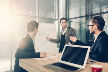 Aufkleber - Serene man demonstrating scheme to young colleagues while standing near it. They sitting at table in office. Presentation concept