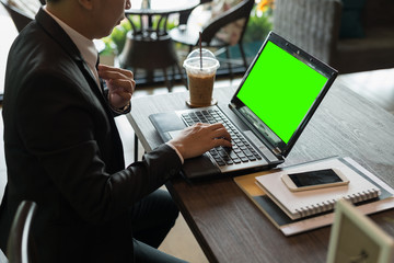 Poster - asian young businessman working on laptop with blank green screen in coffee shop while checking e-mail