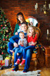 © Tortuga - happy family in a room near a festive Christmas tree, sitting on a chair and embracing.